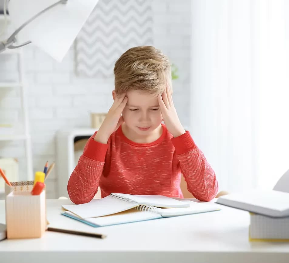 Un enfant découragé, la tête entre les mains devant son cahier